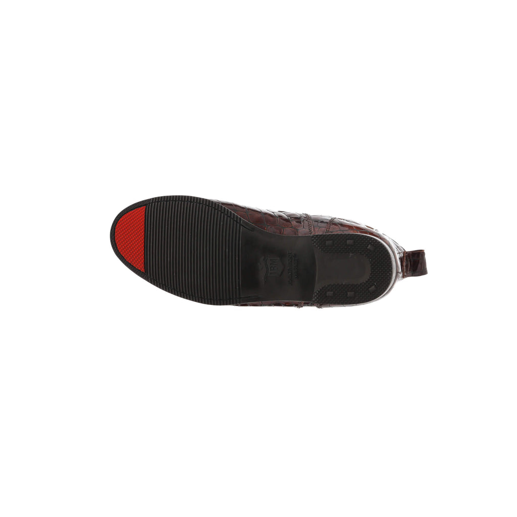 A brown crocodile boot displayed against a white background, laid flat to showcase its sole with a distinctive red tip, representing the signature sole design.