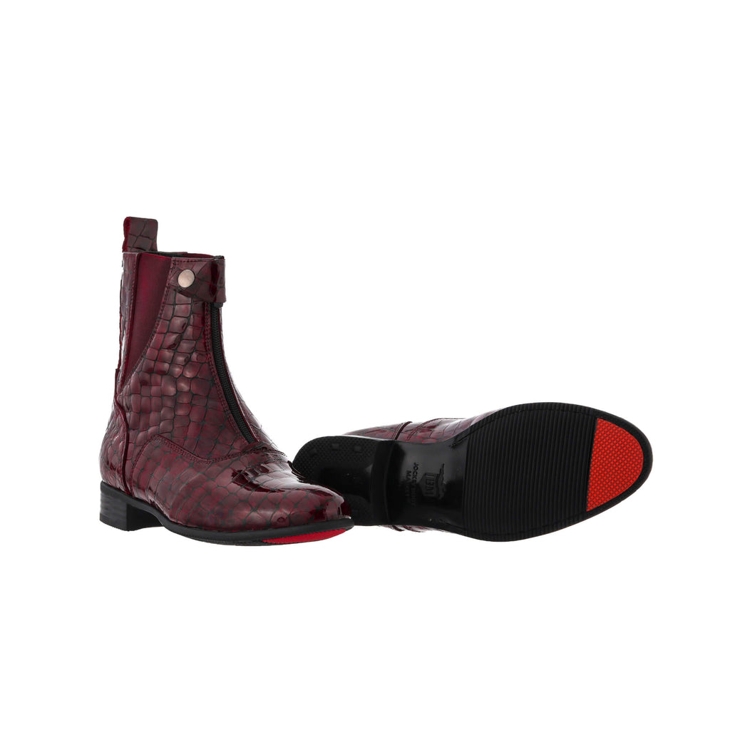 A pair of burgundy crocodile boots displayed against a white background. One boot is positioned sole-down with the buckle and front zip closure completed. The other boot is laid flat to showcase its sole, featuring a red-tipped signature design.