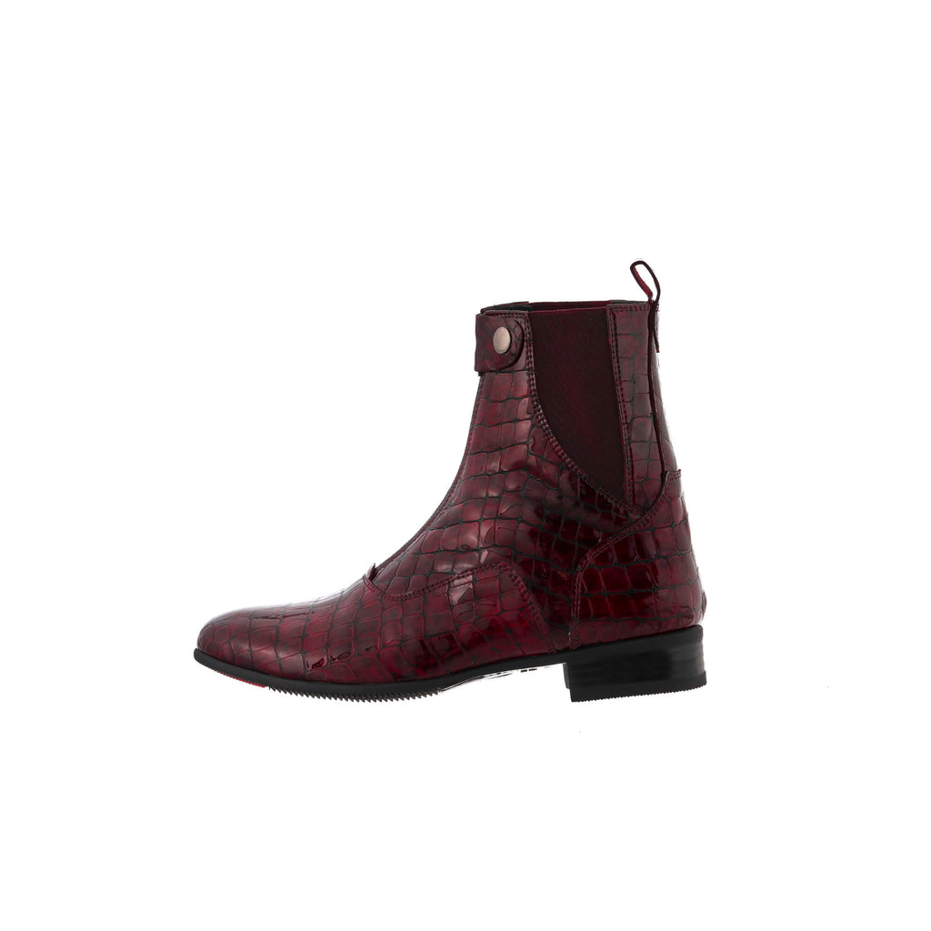 A side view of a burgundy crocodile boot with a front zip and buckle closure, displayed against a white background.